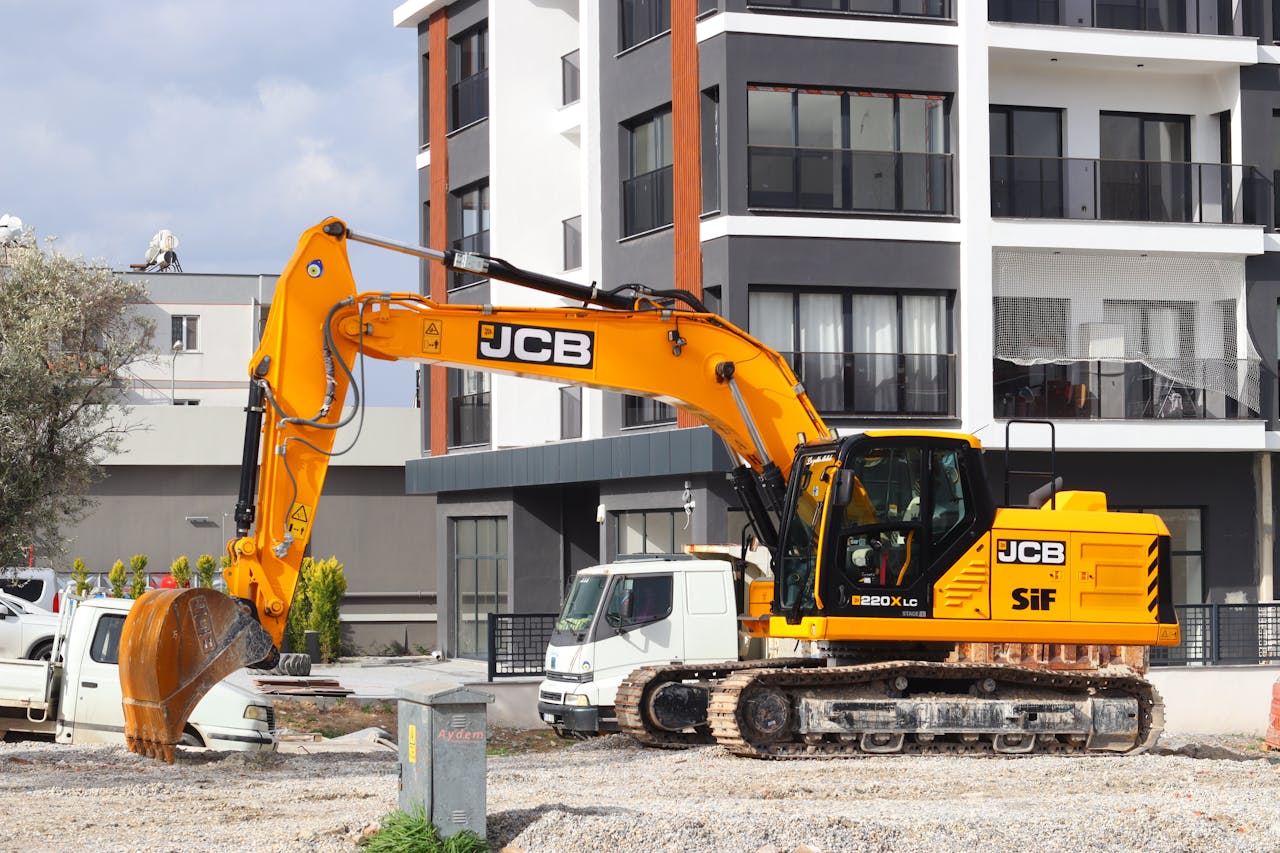 hero-img-02 A yellow excavator operating at a city construction site in front of modern buildings.